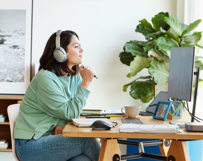 Woman wearing headphones, holding pen and looking at a PC monitor